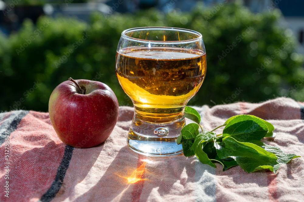 Glass of apple cider drink in sunlights and houses of Etretat village on background, Normandy, France Glass of apple cider drink in sunlights and houses of Etretat village on background, Normandy, France