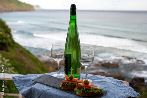 Txakoli or chacolí slightly sparkling very dry white wine produced in the Spanish Basque Country, served outdoor with view on Bay of Biscay, Atlantic Ocean. photo