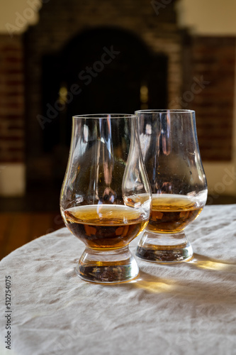 Fototapeta Naklejka Na Ścianę i Meble -  Two glasses of scotch whiskey with view on fireplace in old house on background, Edinburgh whisky tasting tour, Scotland