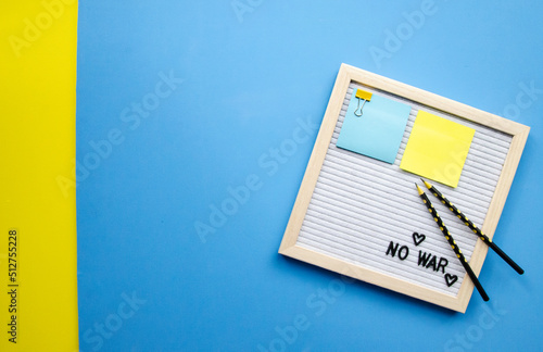 Flatlay horizontal composition empty letter board with the words No War and black pencils, pray for Ukraine patriotic colors blue and yellow sticker, empty blue background