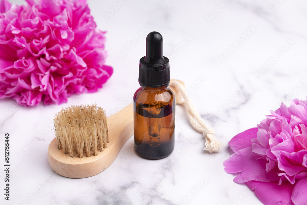 Cosmetic oil in a glass dropper bottle and massage brush on marble background with peonies. Skin care cosmetic. Beauty concept for face body care Cosmetic oil in a glass dropper bottle and massage brush on marble background with peonies. Skin care cosmetic. Beauty concept for face body care
