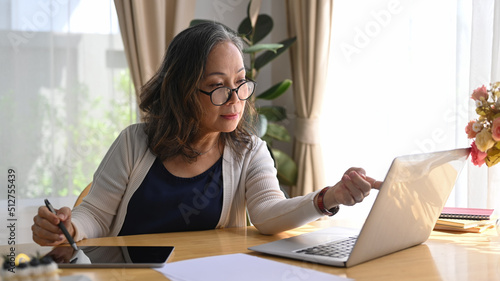 Concentrated mature businesswoman working from home  having online video call on laptop while sitting in modern home