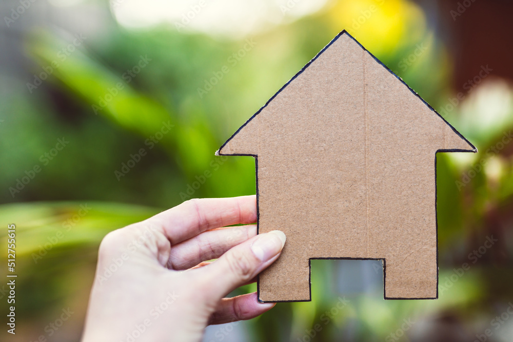 hand holding house icon in front of backyard bokeh, concept of real estate or dream home or family life hand holding house icon in front of backyard bokeh, concept of real estate or dream home or family life