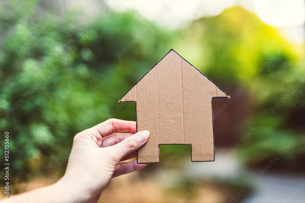 hand holding house icon in front of backyard bokeh, concept of real estate or dream home or family life hand holding house icon in front of backyard bokeh, concept of real estate or dream home or family life