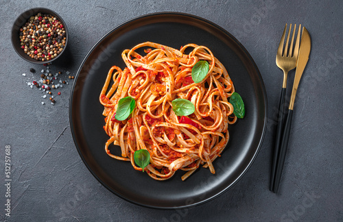 Italian linguini pasta with tomato sauce in a black plate on a dark background. Top view, close-up.