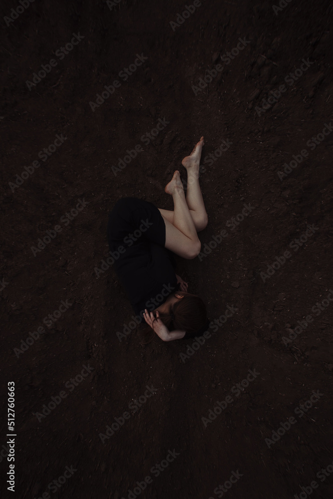 young teen girl in black dress is lying sad in the pose of a baby on the ground background and crying. top view. poster social concept, free space young teen girl in black dress is lying sad in the pose of a baby on the ground background and crying. top view. poster social concept, free space