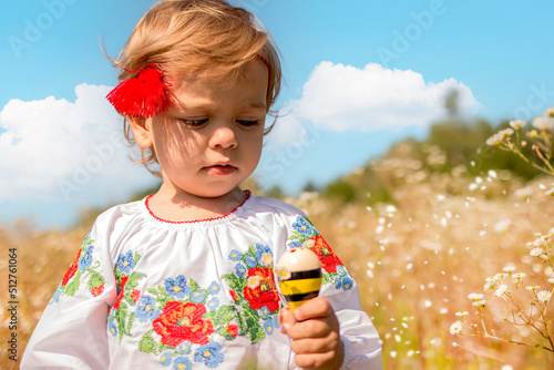 Fotografie, Tablou Funny little Ukrainian Caucasian girl in a shirt with embroidery playing in nature where wild flowers