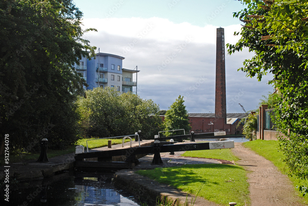 Quiet Canal with Lock Gates and Towpath with Tall Industrial Brick Chimney seen against Cloudy Sky 