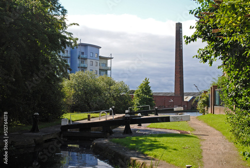 Quiet Canal with Lock Gates and Towpath with Tall Industrial Brick Chimney seen against Cloudy Sky  photo
