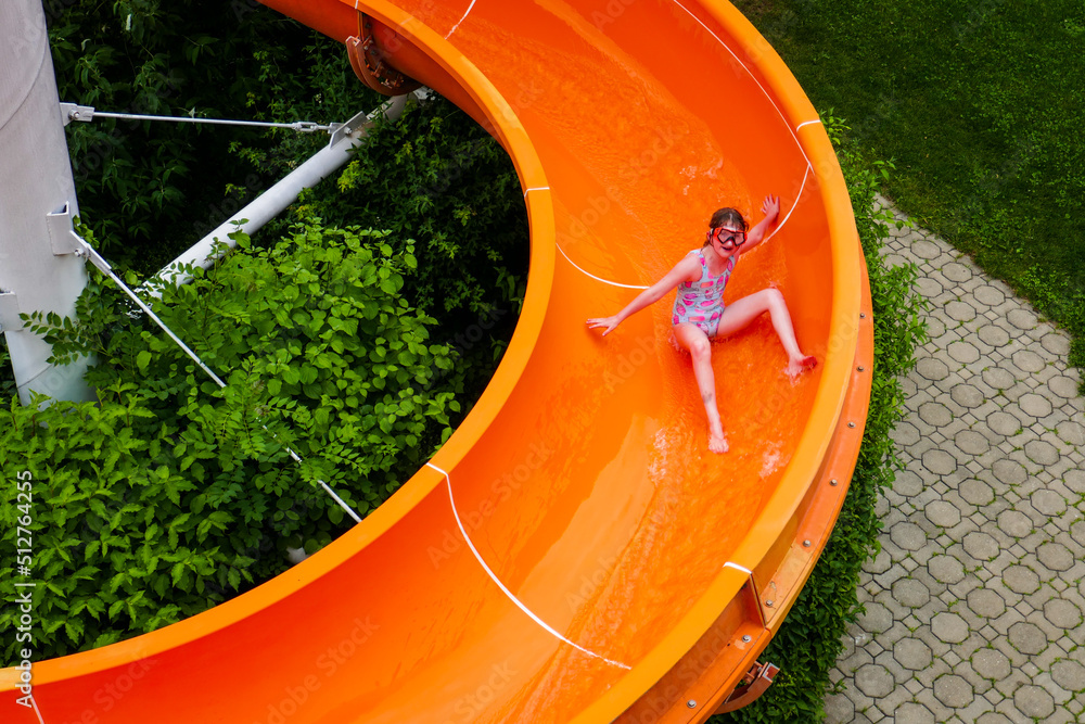 The girl swims in the pool in the water park. Children swim on the water slide.