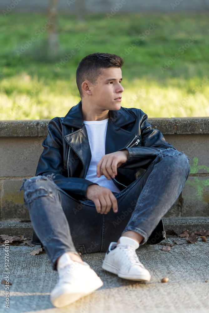 Obraz premium Young happy boy teenager sitting on floor in front of the camera in posed portrait