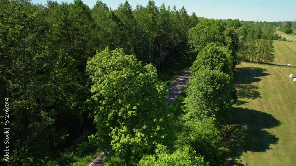 Flying over a Countryside Road Next to a Green Field and Forest Trees Park, Woodland and Landscape of Rural Area in Poland at Beautiful Summer Day Flying over a Countryside Road Next to a Green Field and Forest Trees Park, Woodland and Landscape of Rural Area in Poland at Beautiful Summer Day