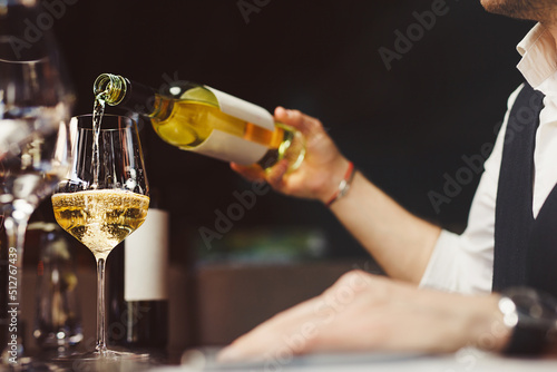 Quadro su tela Bartender pouring sparkling white wine into wineglasses.