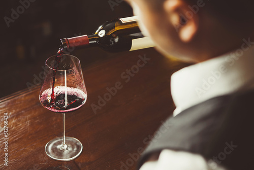 Close-up photo  sommelier pours red wine to glass on bar counter background.