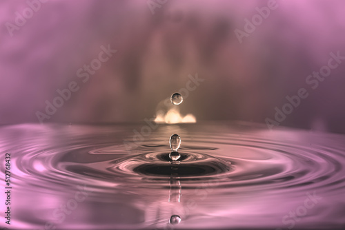 Water drop falling on water surface created ripples on pale purple shadow light background.