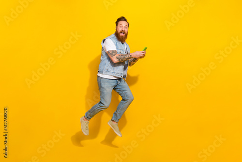 Full body photo of overjoyed sporty man hold telephone jumping isolated on yellow color background