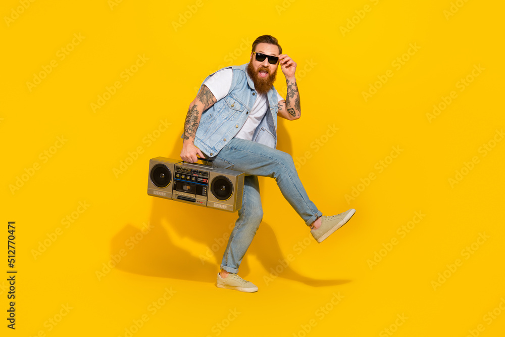 Photo of cool charming man wear jeans waistcoat arm dark eyewear dancing listening boom box isolated yellow color background Photo of cool charming man wear jeans waistcoat arm dark eyewear dancing listening boom box isolated yellow color background