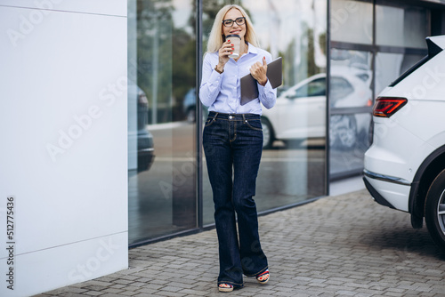 Female aged car dealership drinking coffee outside car showroom