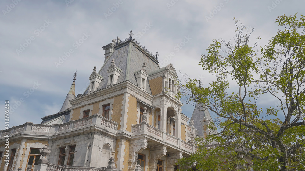 Beautiful facade of European palace on background of trees and sky. Action. Yellow palace in European style with garden. Massandra Palace in Crimea