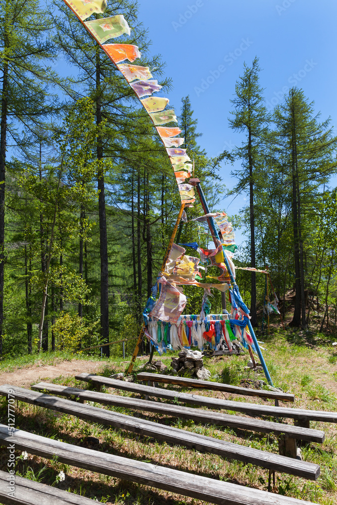 Buddhist place in Buryatia on hill above confluence of Black and White Irkut rivers with colored ribbons of pilgrims and prayer flags with Buddhist mantras. Wooden benches for pilgrims in forest glade