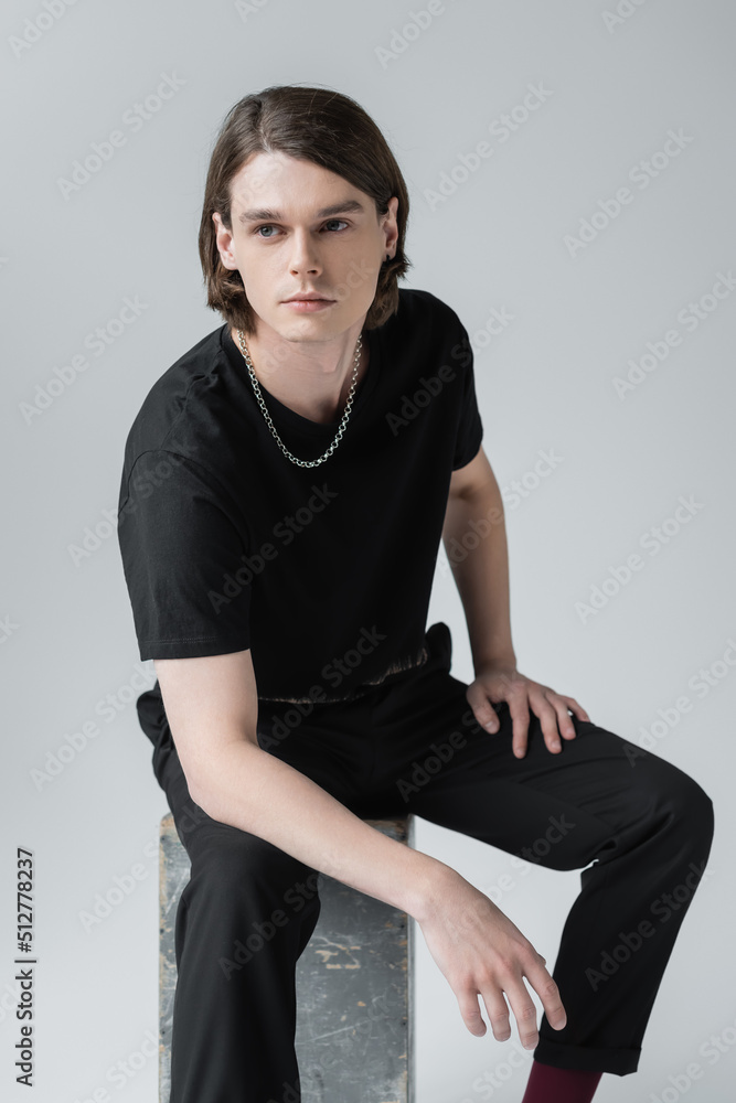 Stylish young man looking away while sitting on concrete block isolated on grey. Stylish young man looking away while sitting on concrete block isolated on grey.