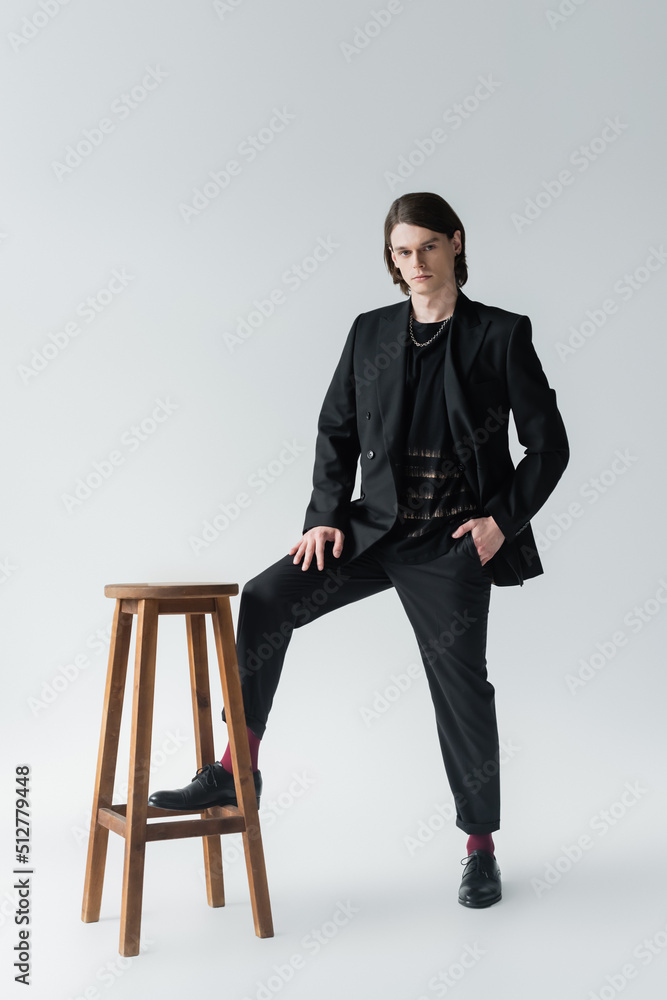 Full length of stylish man in suit posing near chair on grey background. Full length of stylish man in suit posing near chair on grey background.