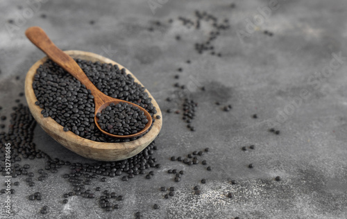 Bowl of dry black lentils beans with a spoon on grey table close up, protein source for vegetarian diet