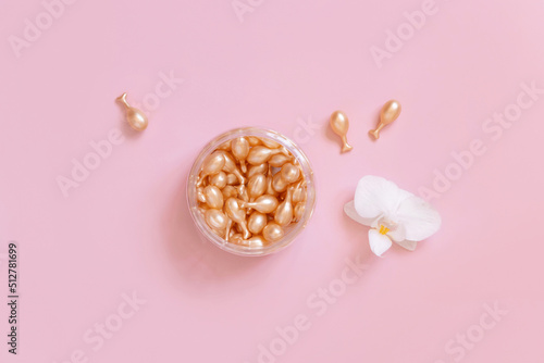Face serum capsules in a jar near orchid flower on light pink top view. Cosmetics, beauty product