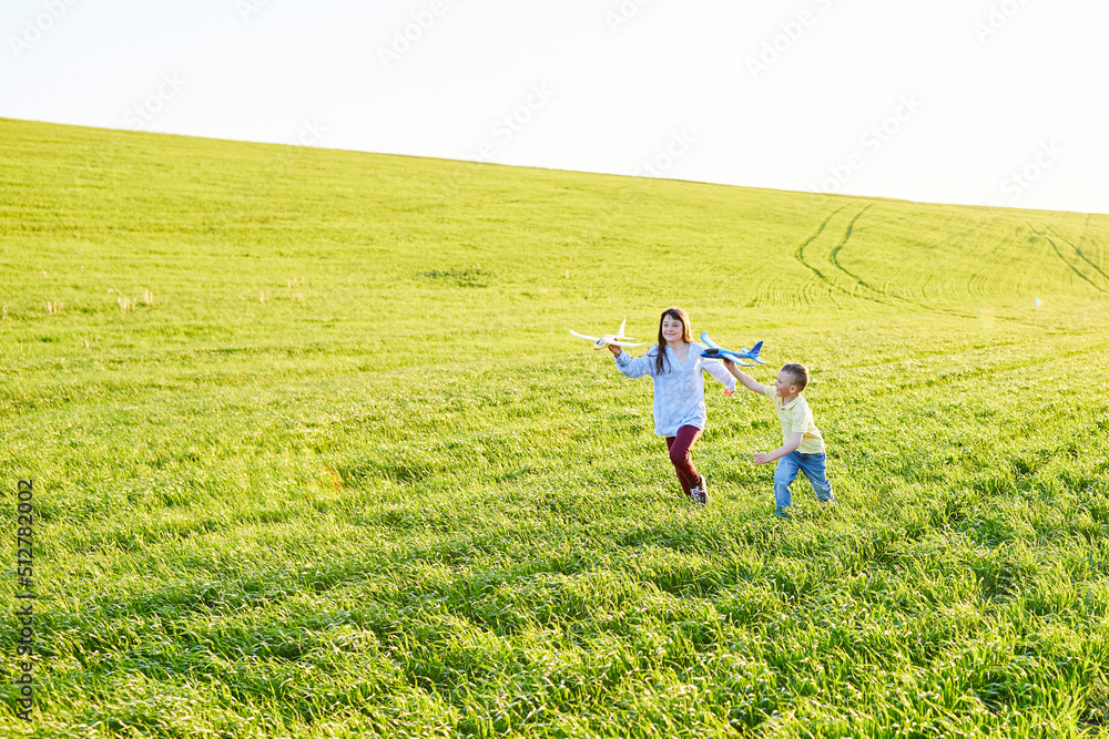 Cheerful and happy children play in the field and imagine themselves to be pilots on a sunny summer day. Kids dreams of flying and aviation.