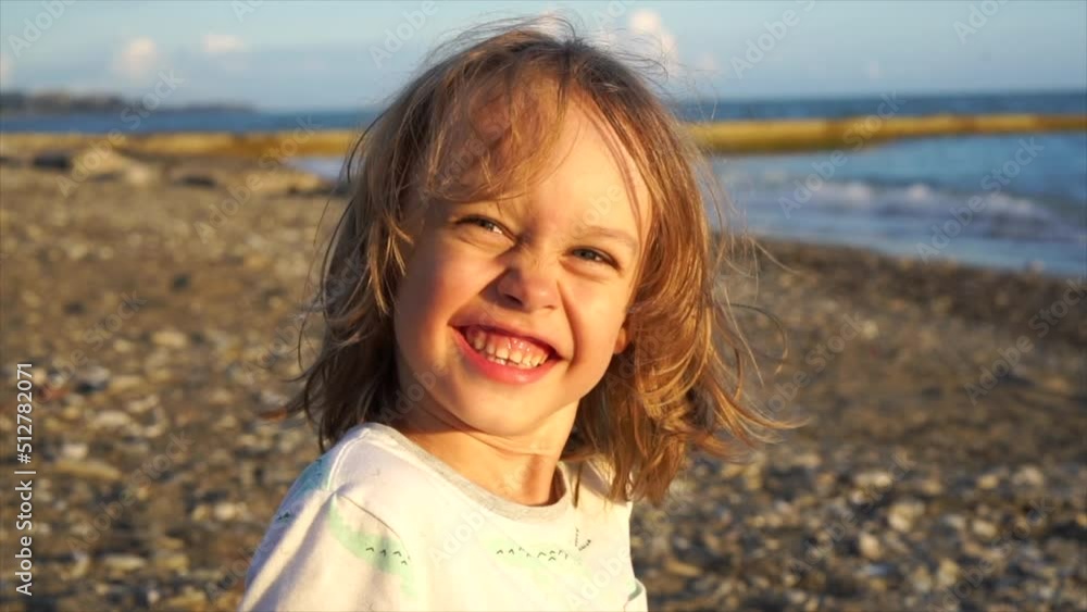 Portrait of a cute boy with long hair looking at the camera, smiling and squinting at the sun during sunset on the sea. Handheld shot. Slow Motion. Portrait of a cute boy with long hair looking at the camera, smiling and squinting at the sun during sunset on the sea. Handheld shot. Slow Motion.