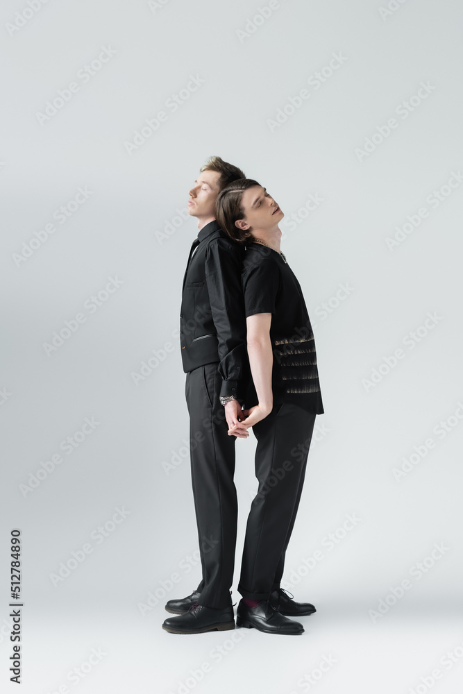 Full length of same sex couple holding hands on grey background. Full length of same sex couple holding hands on grey background.