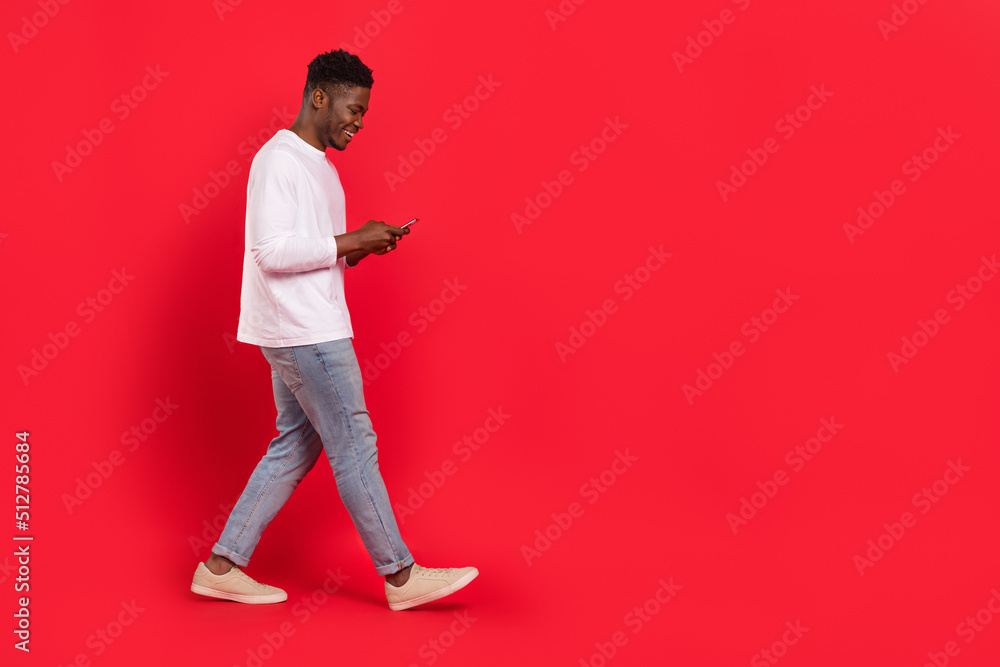 Full size profile portrait of cheerful person walk use telephone chatting isolated on red color background Full size profile portrait of cheerful person walk use telephone chatting isolated on red color background