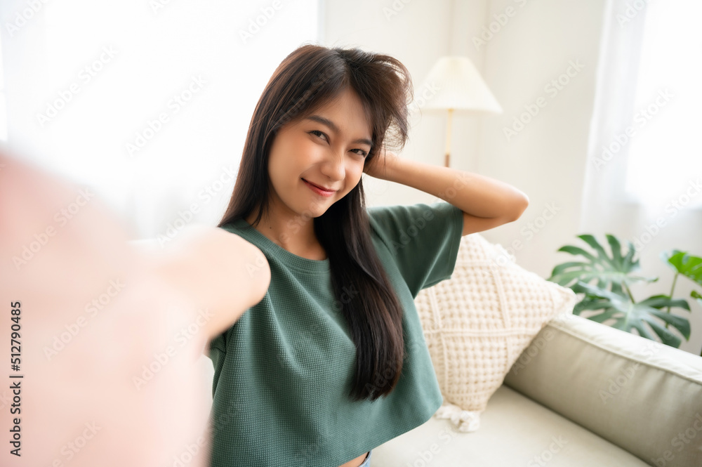 Pretty young asian female with big smile sitting at living room. She having fun taking light cheerful selfie on blurred background Pretty young asian female with big smile sitting at living room. She having fun taking light cheerful selfie on blurred background