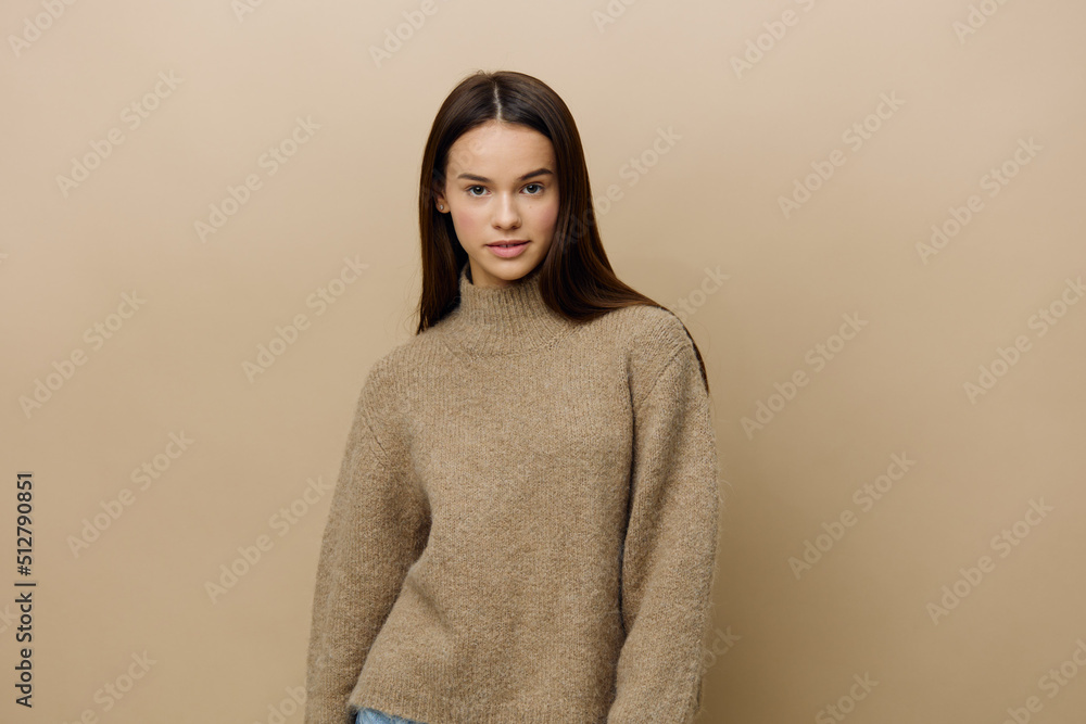 a beautiful, young, attractive woman with long, well-groomed hair stands in a warm textured sweater on a beige background, posing with her hands in a relaxed manner and looking affably into the camera a beautiful, young, attractive woman with long, well-groomed hair stands in a warm textured sweater on a beige background, posing with her hands in a relaxed manner and looking affably into the camera