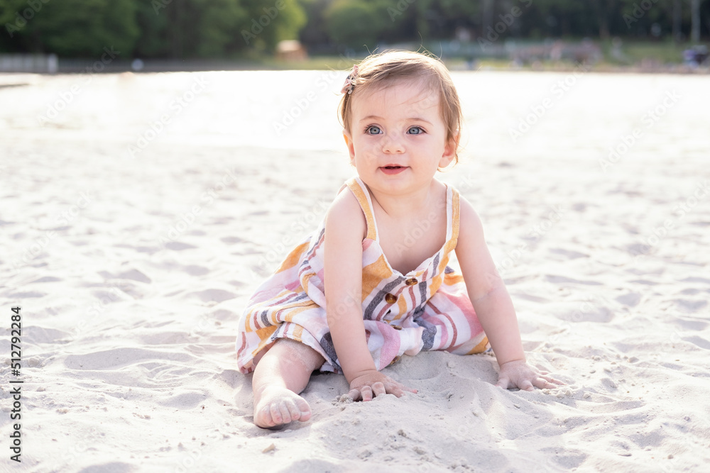 happy baby girl sitting on the beach on sand wearing striped summer dress on sunny day happy baby girl sitting on the beach on sand wearing striped summer dress on sunny day