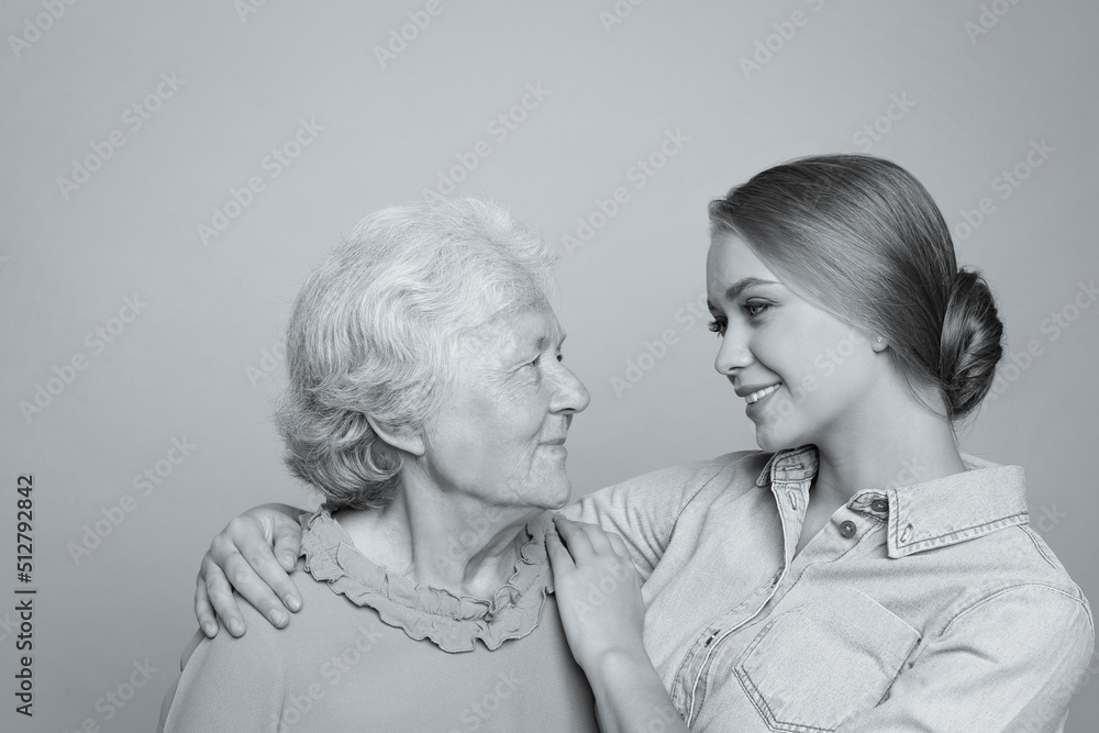 Young woman and her grandmother on light background. Black and white photography