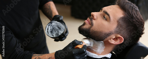 Obraz na plátně Professional hairdresser applying shaving foam onto client's skin in barbershop