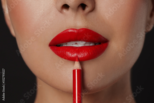 Young woman applying beautiful red lip pencil on black background, closeup