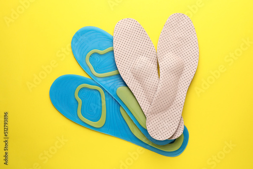 LIght blue and beige orthopedic insoles on yellow background  flat lay
