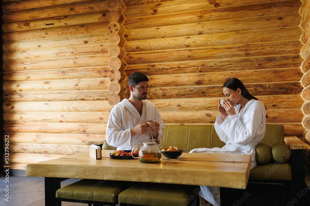 Man and a woman drink tea sitting in a wooden room after a sauna