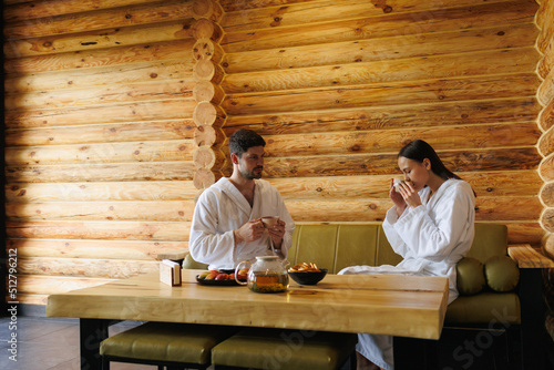 Man and a woman drink tea sitting in a wooden room after a sauna
