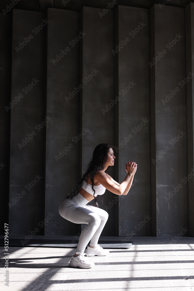 beautiful strong muscular woman practicing sports in gym. Healthy middle-aged adult woman in black sportswear training alone. Fit thin girl doing press indoors, doing squats	