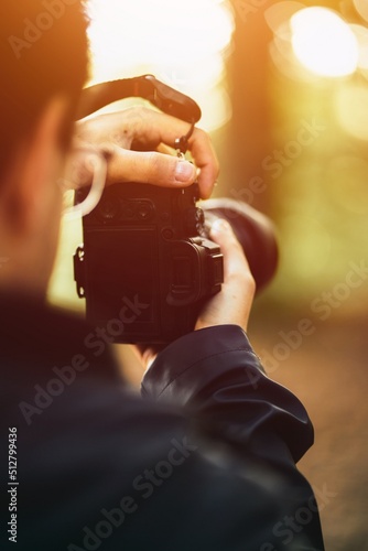 A man holds the mirrorless camera with two hands and the screen is visible. Concept of a hobby photographer taking pictures with a modern digital camera in the woods. photo