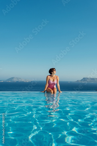 Beautiful young woman swimming in pool and enjoying the epic view over the sea during her summer vacation time.The end of the world. Luxury lifestyle photo of young woman on summer vacation