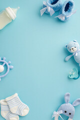Baby boy concept. Top view vertical photo of booties socks soother teddy bear toy teether milk bottle and knitted bunny rattle toy on isolated pastel blue background with empty space in the middle