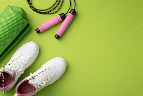 Fitness accessories concept. Top view photo of white sports shoes exercise mat and skipping rope on isolated green background with copyspace