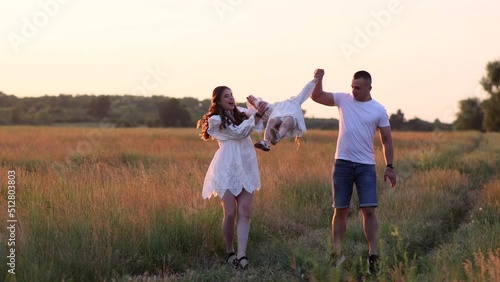 Parents have a fun, play and lift up by the hands their daughter on meadow.
