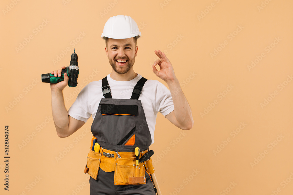Positive male repairman at home holding a screwdriver and showing okay on a beige background Positive male repairman at home holding a screwdriver and showing okay on a beige background