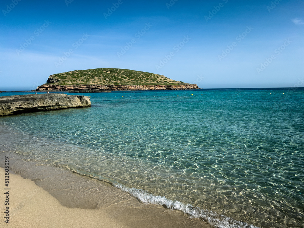 Sunny early morning in Cala Compte beach, Ibiza, with view of little island of Tago Mago. Crystal clear water, turquoise sea, mediterranean summer paradise.