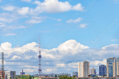 A tall TV tower against a blue sky in an urban summer landscape.